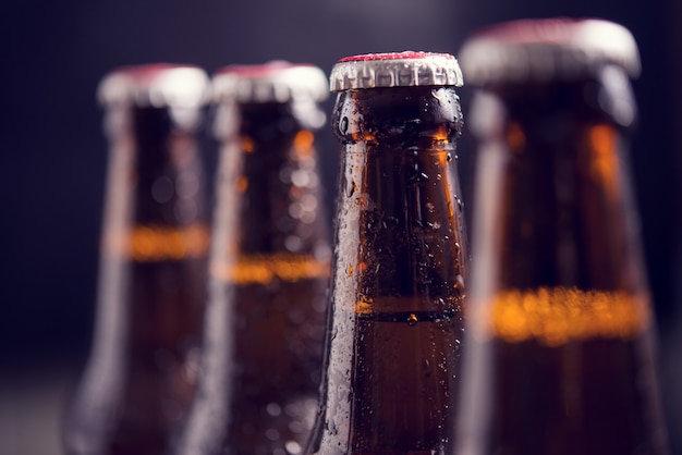 Chiuda sulle bottiglie di vetro di birra con ghiaccio su fondo scuro