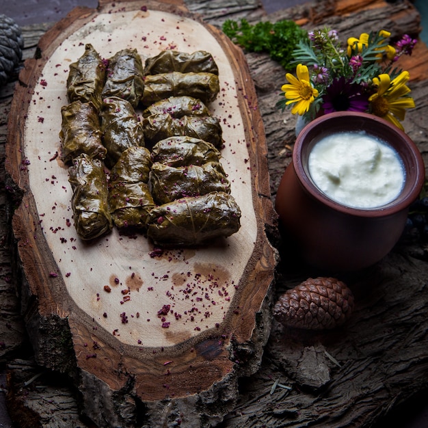 Chiuda sulle foglie dell'uva di dolma farcite con carne e riso con la salsa di panna acida su una tavola di legno scura. cucina tradizionale dell'Europa orientale e asiatica