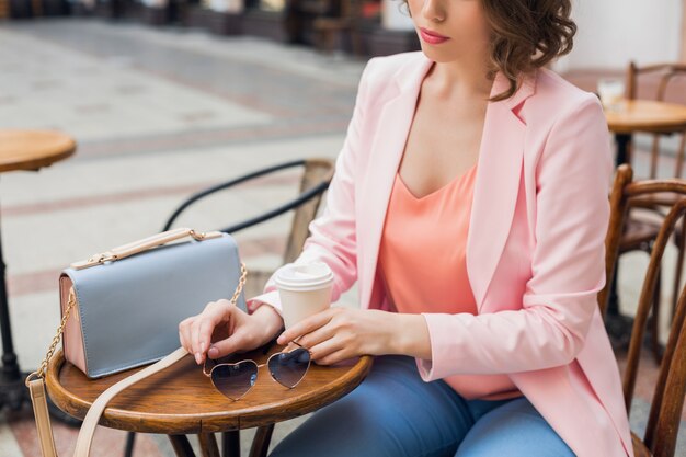 Chiudere i dettagli degli accessori della donna alla moda che si siede nel caffè bevendo caffè, occhiali da sole, borsetta, tendenza moda primavera estate, stile elegante