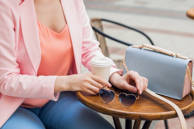 Chiudere i dettagli di accessori di elegante donna seduta da sola in caffè, occhiali da sole, borsetta, colori rosa e blu, tendenza moda primavera estate, stile elegante