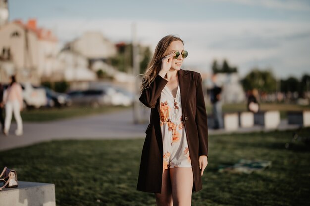 Chiudere l immagine della donna felice in occhiali da sole vestiti in posa lateralmente all'aperto