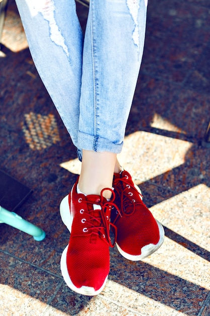 Chiudere l'immagine di moda dei piedi della donna, indossando jeans vintage ed eleganti scarpe da ginnastica rosse, colori dai toni luminosi.