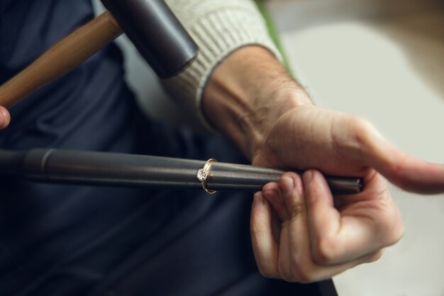 Chiudere le mani del gioielliere, orafi che fanno di anello d'oro con pietre preziose utilizzando strumenti professionali