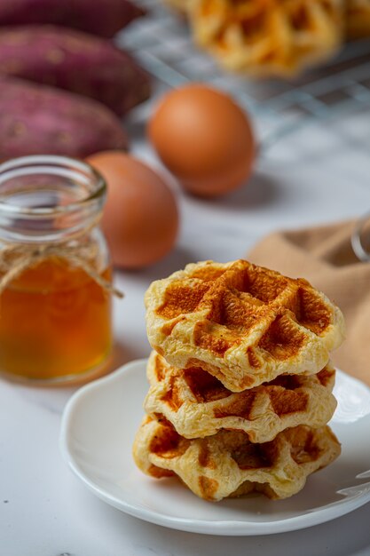 Cialde belghe tradizionali, arance rosse e salsa di mirtilli e tazza di caffè per colazione dolce, composizione su sfondo chiaro.