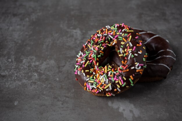 Ciambelle con glassa di cioccolato con spruzza sul tavolo di legno.