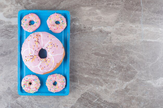 Ciambelle grandi e piccole disposte su un piatto blu su una superficie di marmo