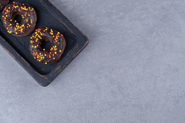 Ciambelle ricoperte di cioccolato e caramelle cosparse su un piatto su una superficie di marmo