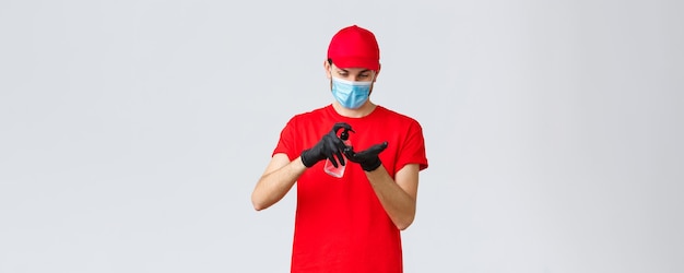 Cibo da asporto e consegna di generi alimentari covid19 concetto di ordini contactless Corriere o dipendente in maglietta rossa e berretto uniforme indossare maschera facciale e guanti di gomma applicare disinfettante per le mani