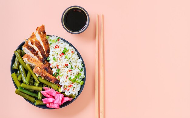 Cibo di strada tradizionale asiatico, pollo croccante con salsa di soia con una porzione di riso, fagiolini, spezie ed erbe aromatiche. Piatto di bacchette fatto in casa pronto da mangiare. Sfondo rosa brillante, layout con spazio di copia