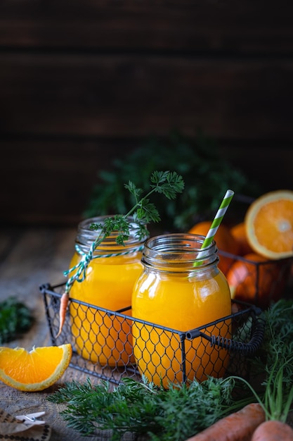 Cibo salutare. Carote e succo di carota con arancia in un barattolo di vetro in un cestino di metallo su uno sfondo di legno scuro. Copia spazio