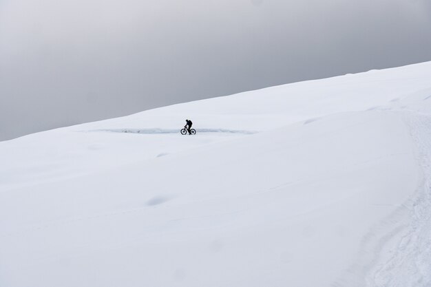 Ciclista completamente attrezzato in sella a una bicicletta in montagne innevate