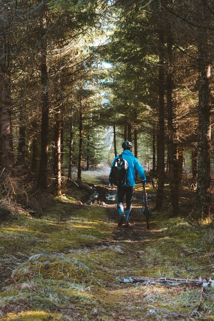 Ciclista in un cappotto blu e un casco nel parco con alberi ad alto fusto