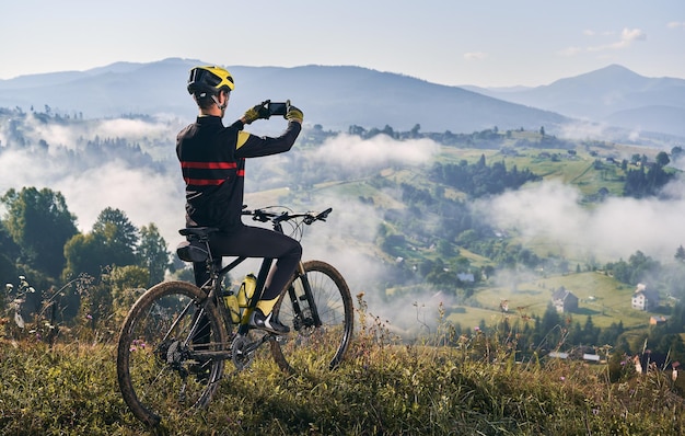 Ciclista maschio che scatta foto di montagna con lo smartphone