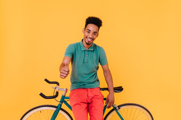 Ciclista maschio di buon umore che posa con il pollice in su. Ritratto dell'uomo felice del brunette che propone con la bicicletta.