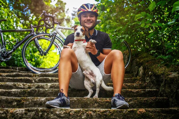 Ciclista maschio in posa con il suo cane russel sulle scale in una foresta.