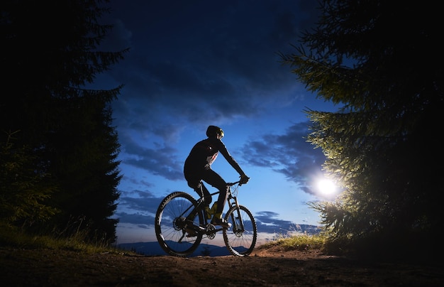 Ciclista maschio seduto in bicicletta sotto il bel cielo notturno
