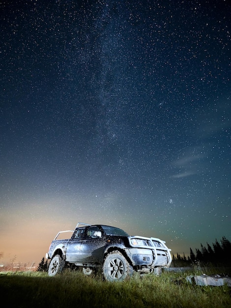 Cielo stellato di bella notte sopra la collina erbosa con l'automobile
