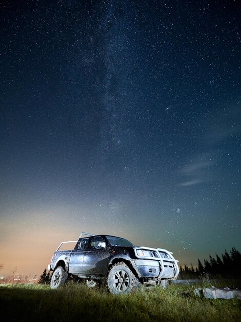 Cielo stellato di bella notte sopra la collina erbosa con l'automobile