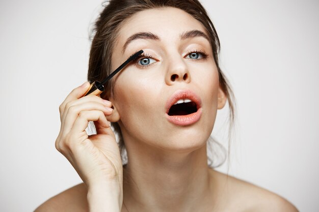 Ciglia di tintura bella ragazza divertente con la bocca aperta guardando la telecamera su sfondo bianco. Concetto di salute e cosmetologia di bellezza.