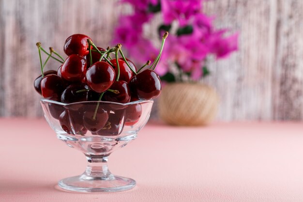 Ciliege con vaso di fiori in un vaso su superficie rosa e sgangherata, vista laterale