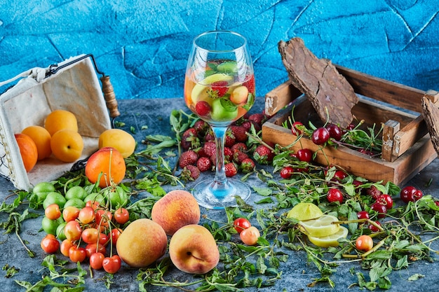 Ciliege fresche rosse sulla scatola di legno con un bicchiere di succo di frutta e frutta fresca