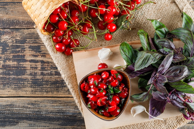 Ciliegia in cestini con marmellata, aglio, basilico, tagliere vista dall'alto su legno e pezzo di sacco