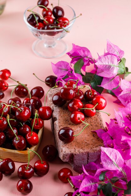 Ciliegie con fiori, mattoni in lamiera di legno e vaso sulla superficie rosa