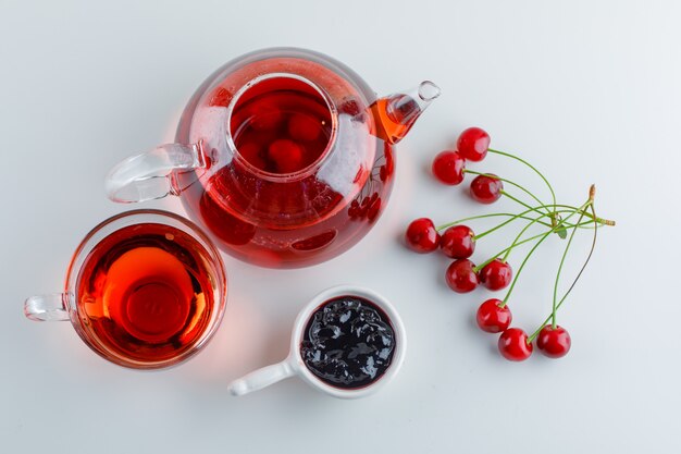 Ciliegie con tè, marmellata su spazio bianco, piatto disteso.