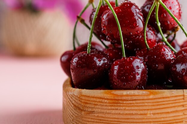 Ciliegie in un piatto di legno con vaso di fiori close-up su una superficie rosa