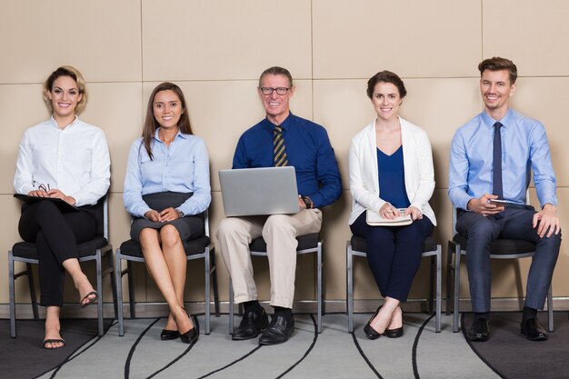 Cinque candidati, sorridente, seduta nella sala di attesa