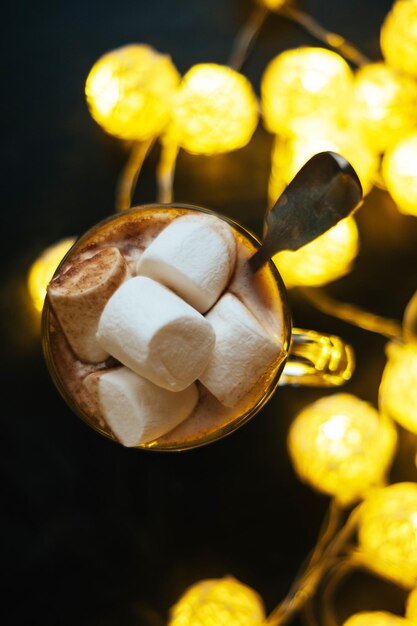 Cioccolata calda in vetro con grandi marshmallow e luci gialle su sfondo nero Punto superiore