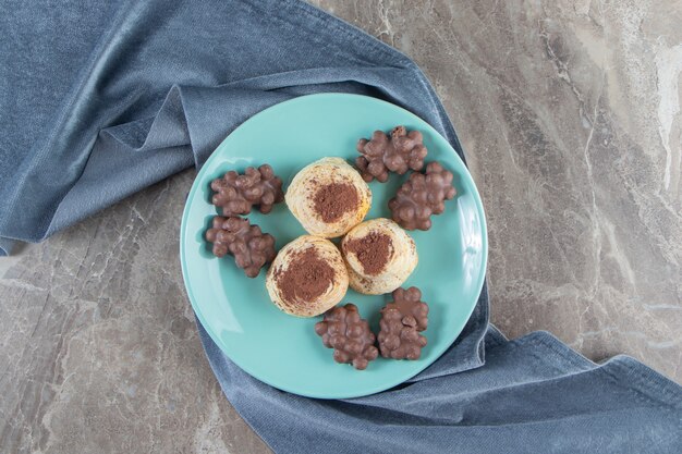 Cioccolato alla nocciola e cacao in polvere sui biscotti su un piatto su un asciugamano sul blu.