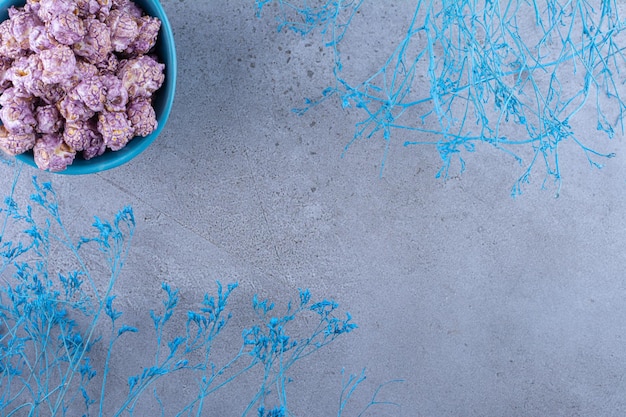 Ciotola blu di popcorn candito accanto a rami decorativi blu sulla superficie in marmo