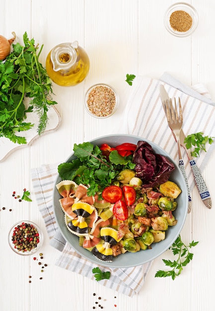 Ciotola con pasta Farfalle, cavoletti di Bruxelles con pancetta e insalata di verdure fresche. Disteso. Vista dall'alto