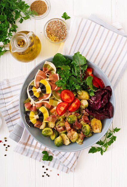 Ciotola con pasta Farfalle, cavoletti di Bruxelles con pancetta e insalata di verdure fresche. Disteso. Vista dall'alto