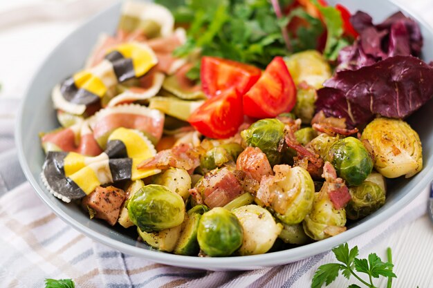 Ciotola con pasta Farfalle, cavoletti di Bruxelles con pancetta e insalata di verdure fresche