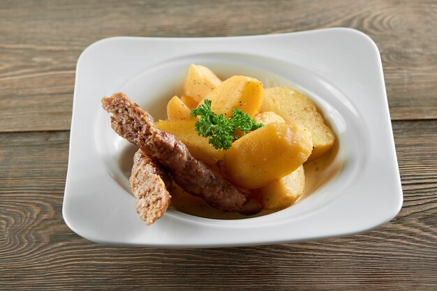 Ciotola da ristorante servita con fette di patate fritte dorate, salsiccia sottile e decorata con foglie di prezzemolo. Sembra molto delizioso e nutriente.