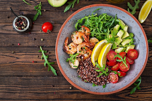 Ciotola di Buddha sano delizioso con gamberetti, pomodoro, avocado, quinoa, limone e rucola sul tavolo di legno. Cibo salutare. Vista dall'alto. Disteso.