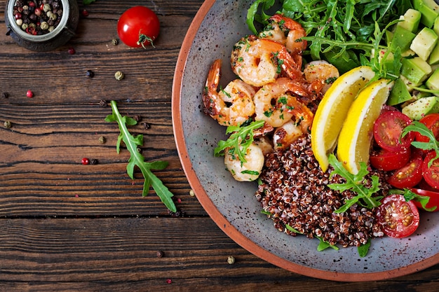 Ciotola di Buddha sano delizioso con gamberetti, pomodoro, avocado, quinoa, limone e rucola sul tavolo di legno. Cibo salutare. Vista dall'alto. Disteso.