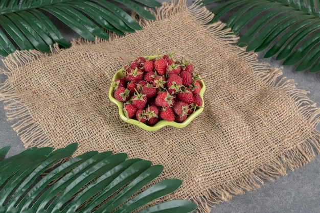 Ciotola di fragole rosse su tela con foglie. Foto di alta qualità