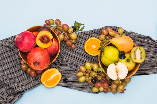 Ciotola di frutta e uva sul tessile su sfondo blu