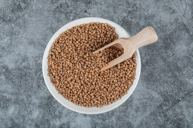 Ciotola di grano saraceno crudo su superficie di marmo