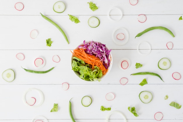 Ciotola di insalata spalmata con la rapa; cetriolo; fette di cipolla con fagiolini sulla scrivania in legno