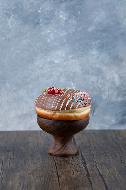 Ciotola di legno di gustosa ciambella con glassa di cioccolato e spruzza sulla tavola di legno.