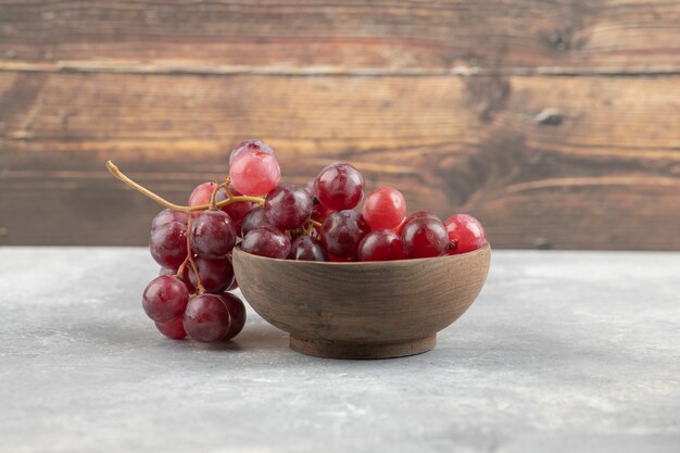 Ciotola di legno di uve rosse fresche sulla superficie in marmo.