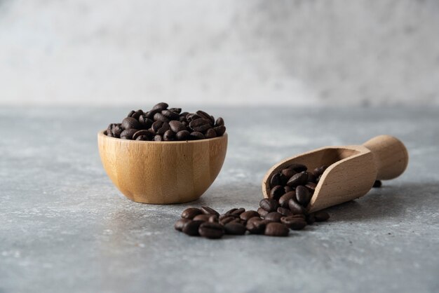 Ciotola di legno e cucchiaio di chicchi di caffè tostati su marmo.