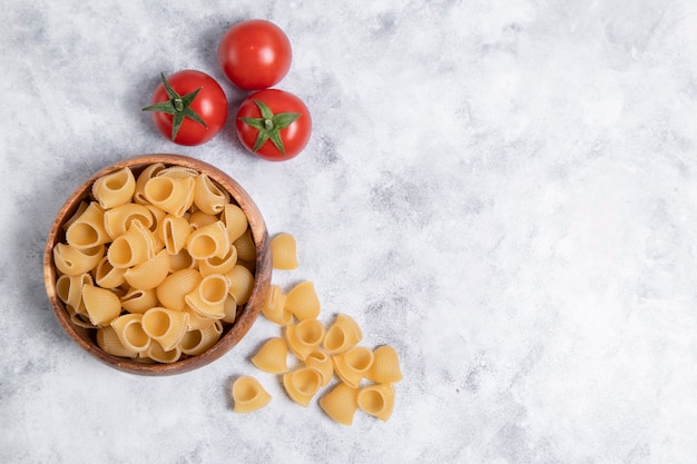 Ciotola di legno piena di pasta cruda Conchiglie poste su sfondo marmo. Foto di alta qualità