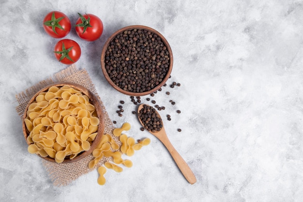 Ciotola di legno piena di pasta secca cruda Farfalle posta sulla tavola di marmo. Foto di alta qualità