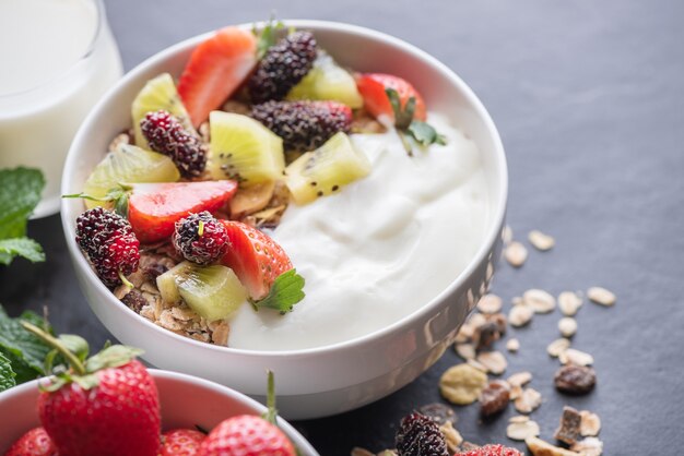 Ciotola di muesli d'avena con yogurt, gelso fresco, fragole, menta kiwi e noci sulla tavola di roccia nera per una sana colazione, spazio copia. Concetto di menu per la colazione sana.