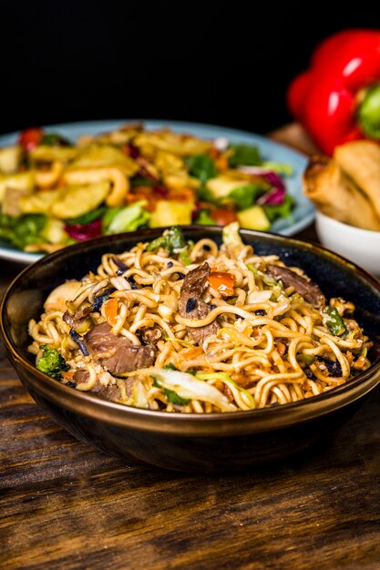 Ciotola di noodles stir fritti con manzo sulla scrivania in legno